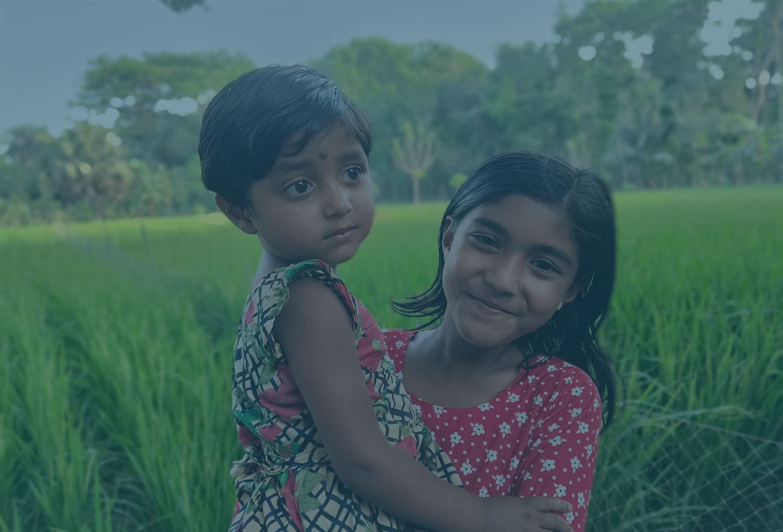 Two smiling girls in a green field in rural Bangladesh