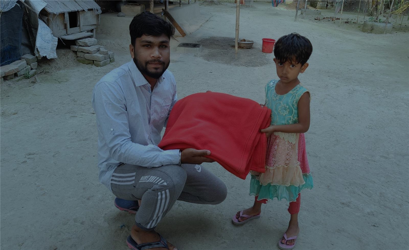 A volunteer kneeling to hand a girl a new blanket in Gonali