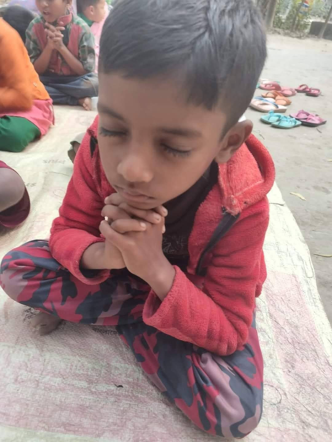 A boy in Gonali, Bangladesh, praying with his hands clasped and eyes closed