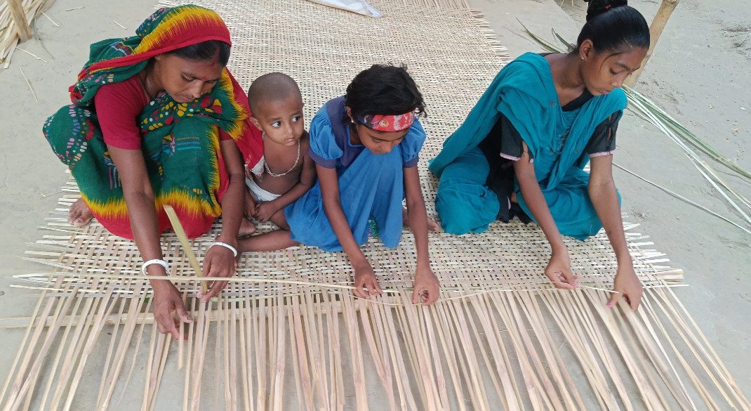 A mother and children weaving a bamboo mat